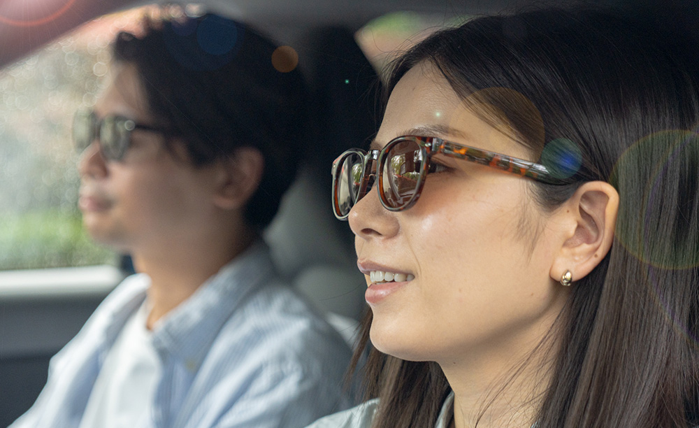 偏光調光グラスを着用して、日差しの強い中を笑顔で快適にドライブを楽しむ男女の様子